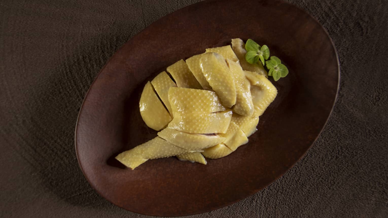 Poached chicken leg quarter in oval wooden dish with green flower garnish