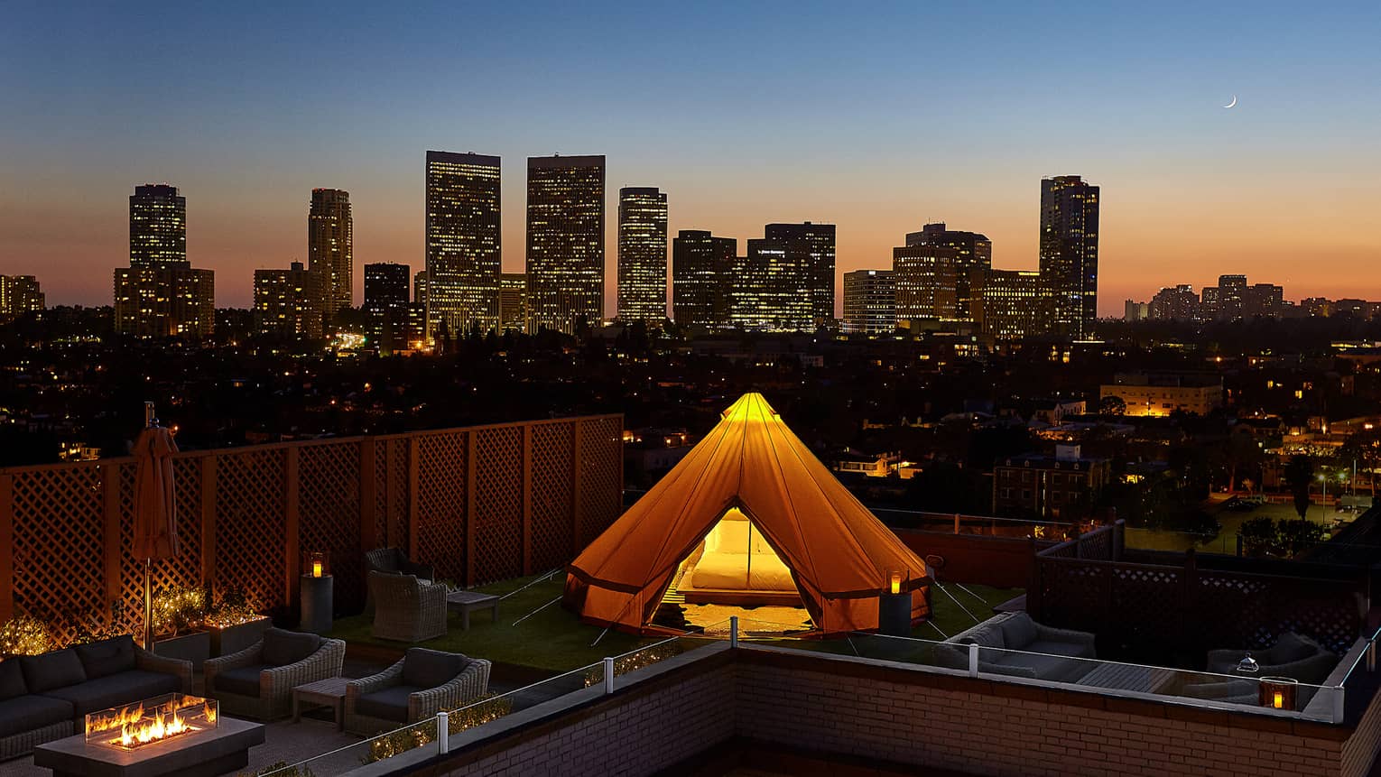 Glowing white tent, bed on rooftop patio by chairs, outdoor fireplace, Beverly Hills sunset city views