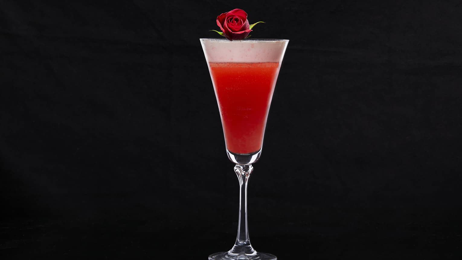 Cocktail glass with red drink and a rose on top.