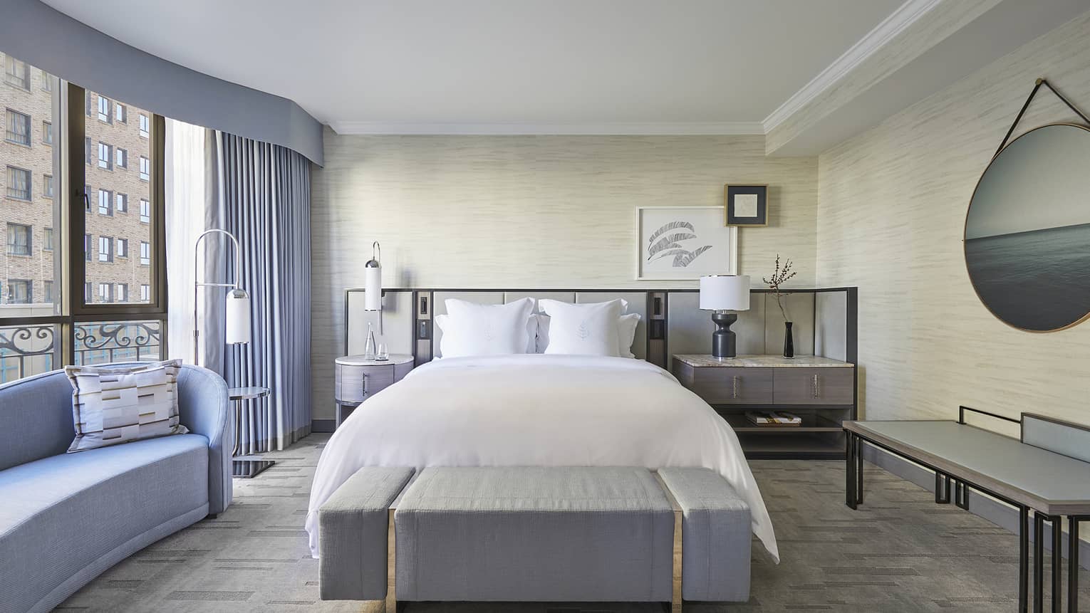 Bedroom with king bed, cushioned bench, chaise, city view