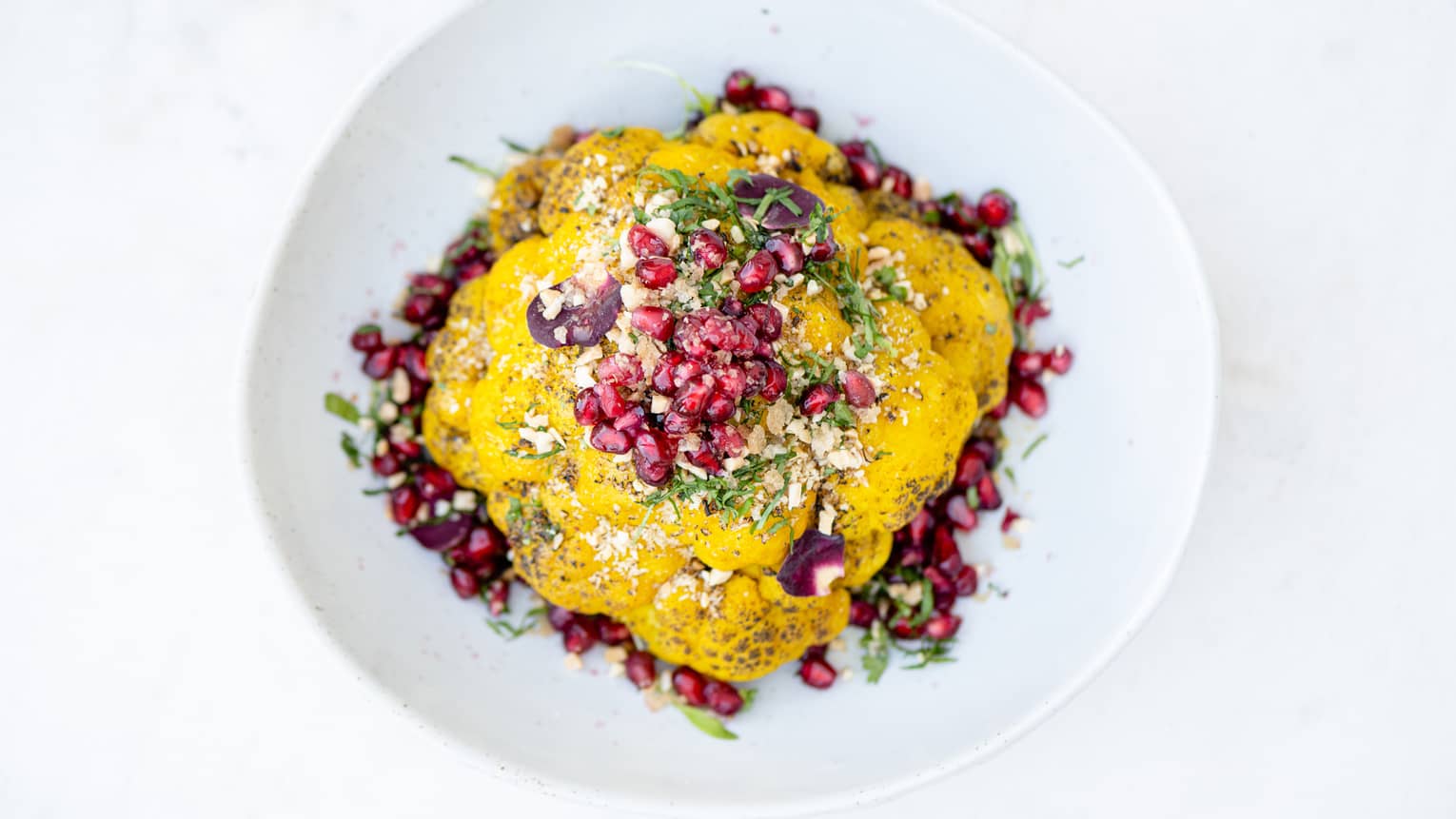 Pomegranate, yogurt, and herbs on a white plate.