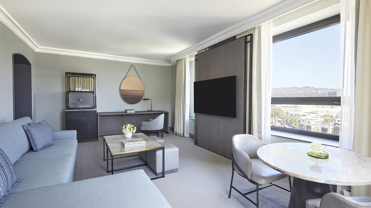 Living room with light blue sofa, table and two chairs, desk and wall-mounted TV