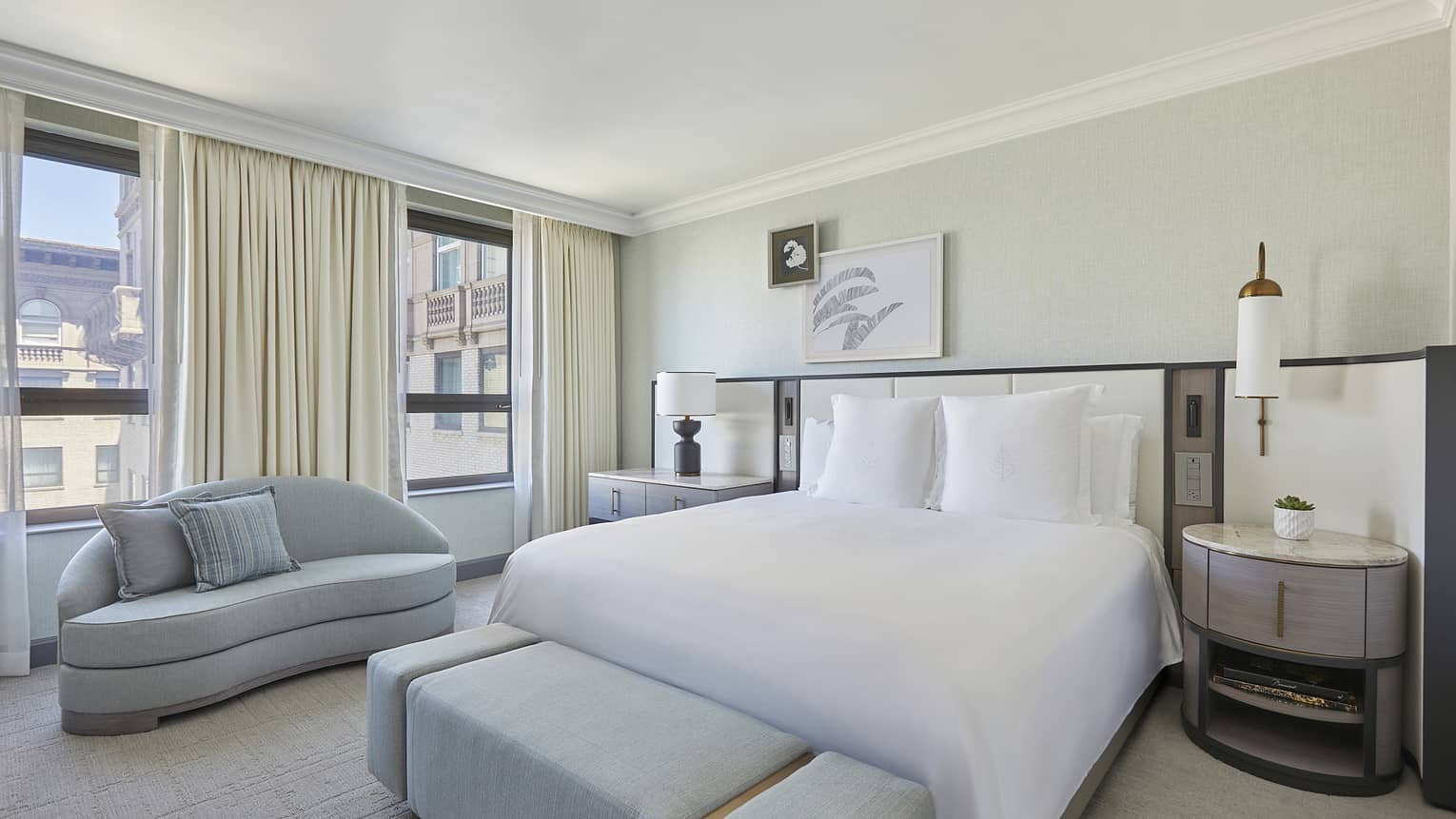 Bedroom with king bed, light grey chaise and bench, windows