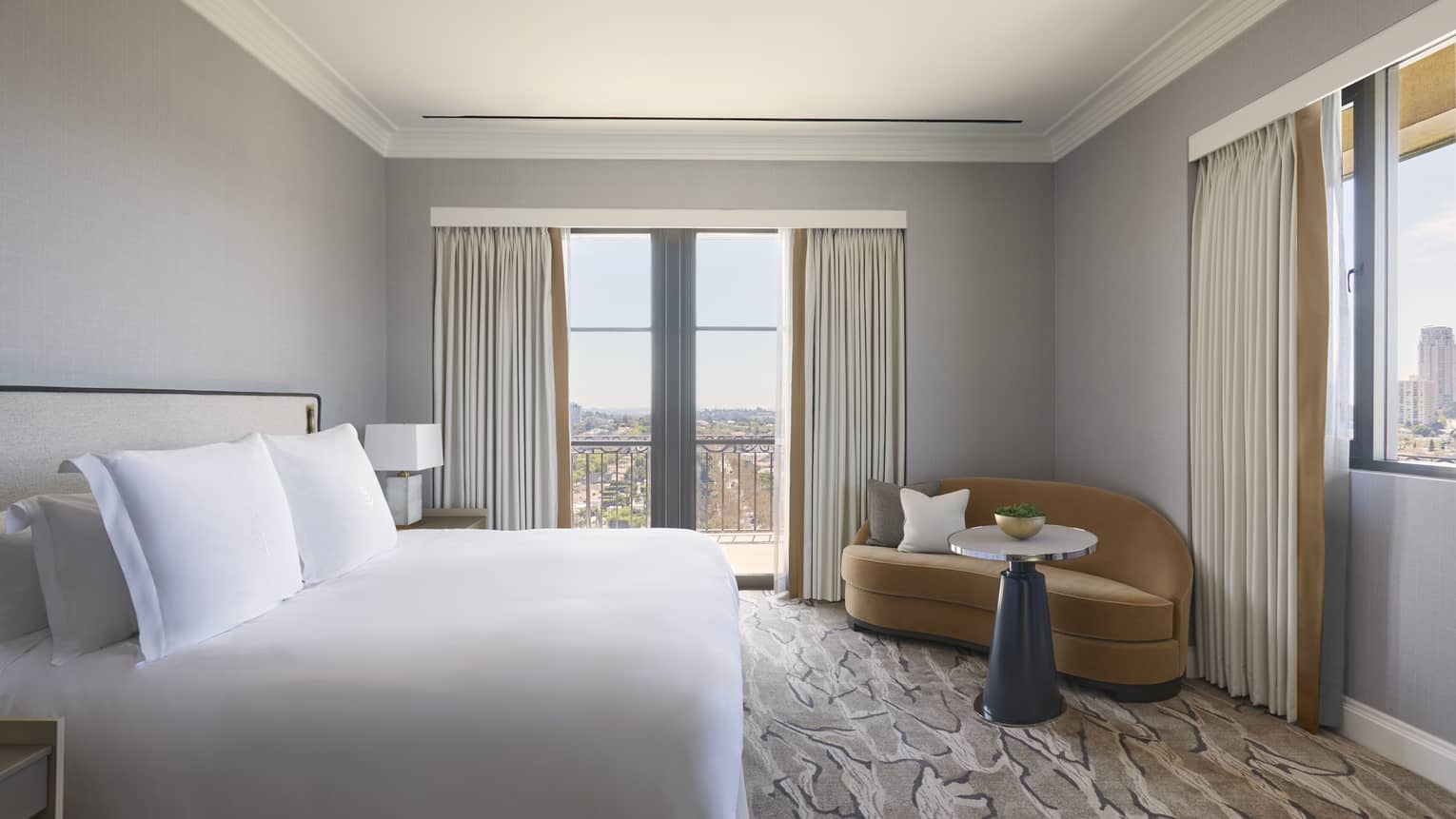 Bedroom with white king bed, tan chaise and small table in the corner, walk-out balcony