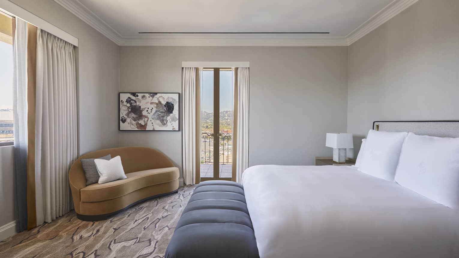 Bedroom with king bed, white sheets, grey cushioned bench, tan chaise and walk-out balcony