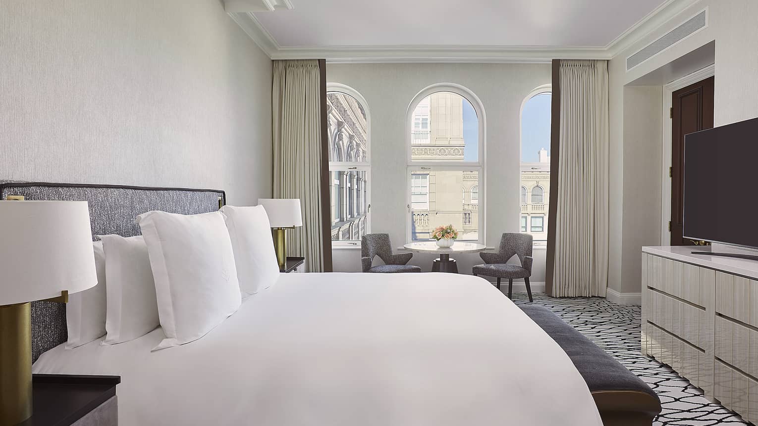 Bedroom with king bed, dresser, TV and small table and two chairs by arched windows