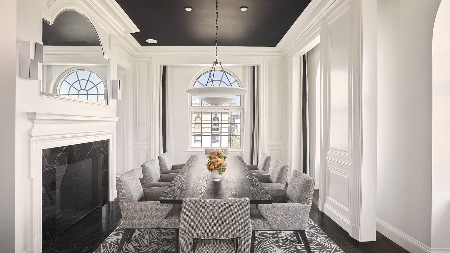 Dining room with fireplace, arched window, and dark wood table with eight grey cushioned chairs