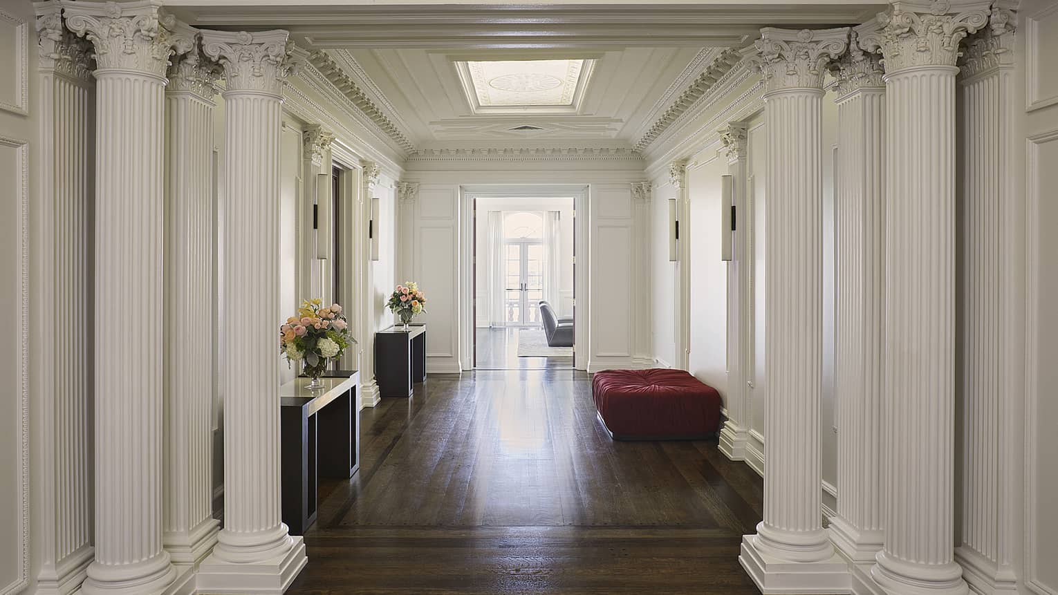 Foyer entry area with white Roman columns, wooden floors and dark red cushioned bench