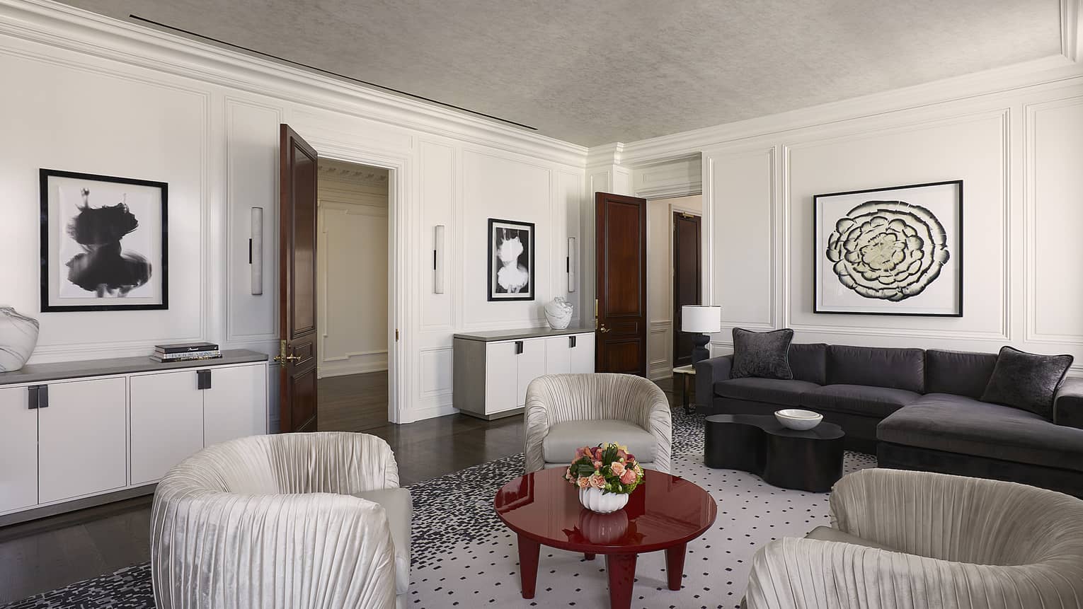 Living room with grey sofa, artwork and three ivory arm chairs positioned around red coffee table