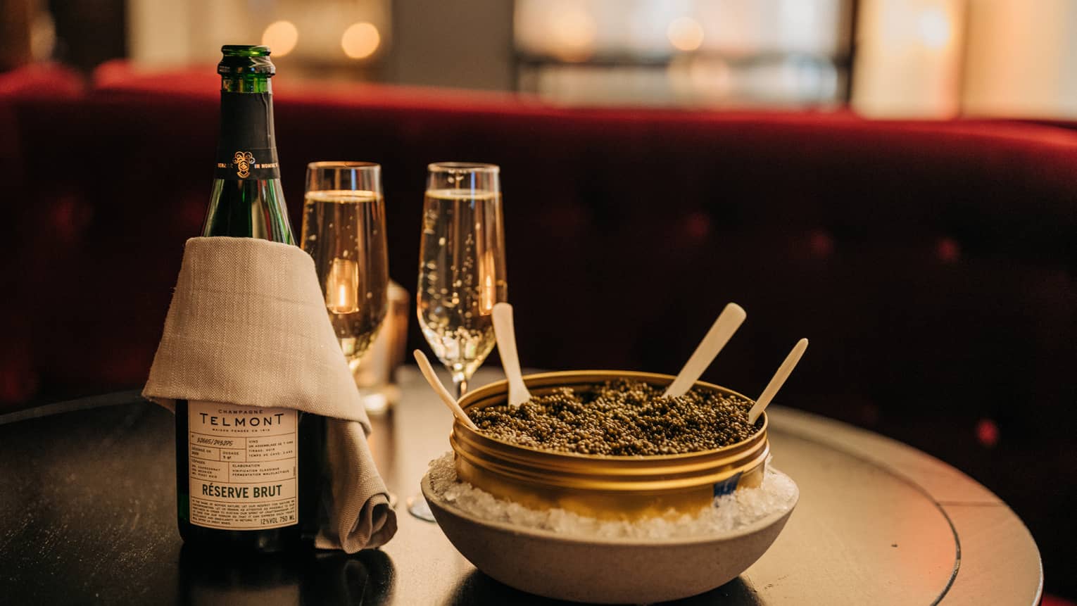 A bowl of caviar beside two champagne glasses and a bottle of champagne