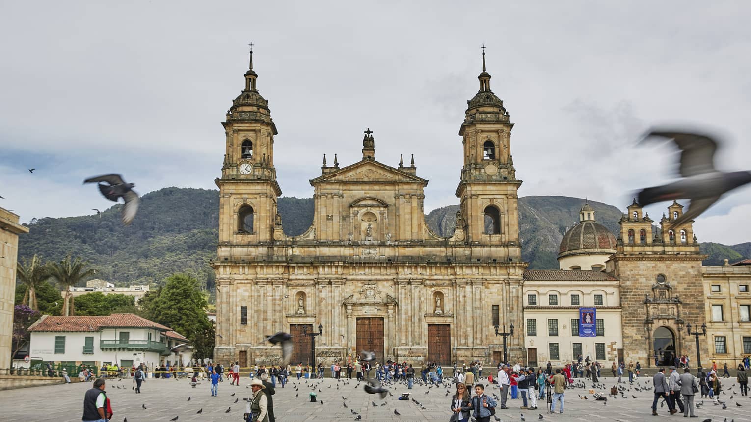 Pigeons fly over crowds in courtyard in front of historic Bogota cathedral