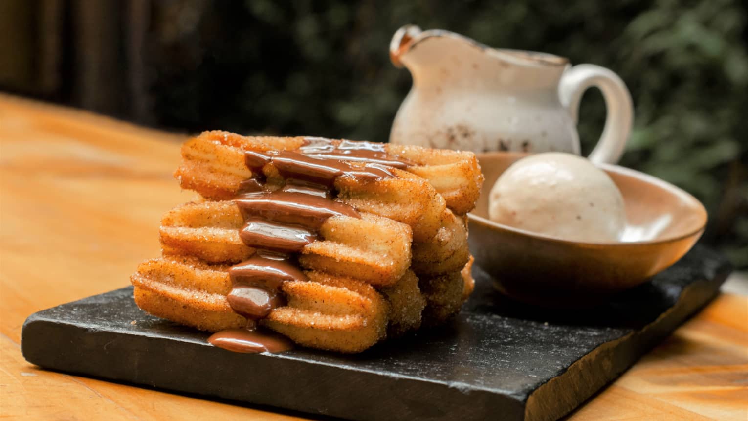 Pastries with chocolate on a black tray with ice cream in a bowl.