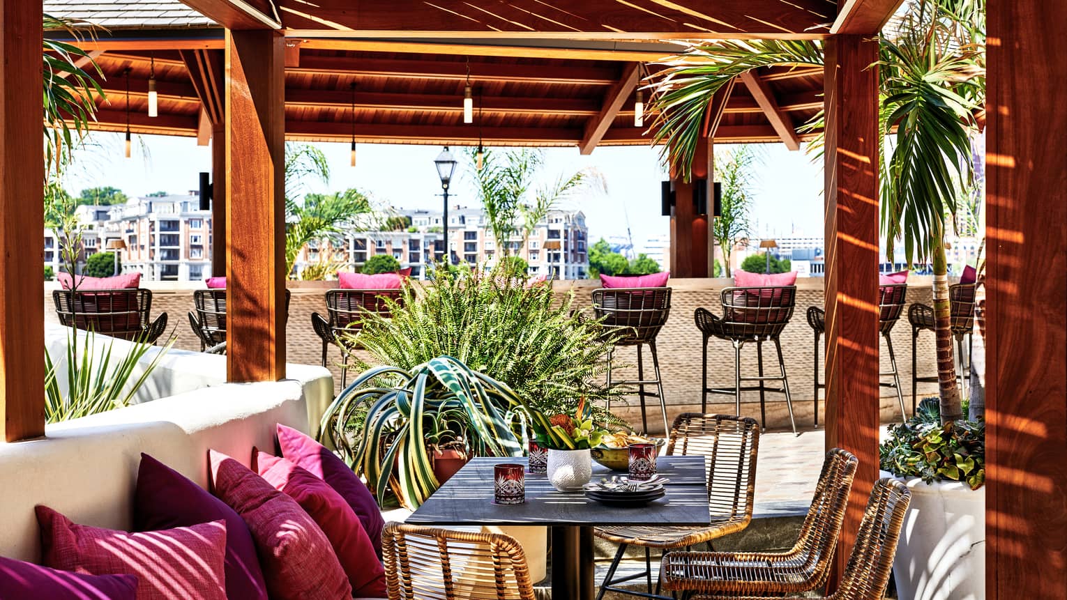 An outdoor eating venue with red cushions on benches and stools surrounded by red pillars and trees.