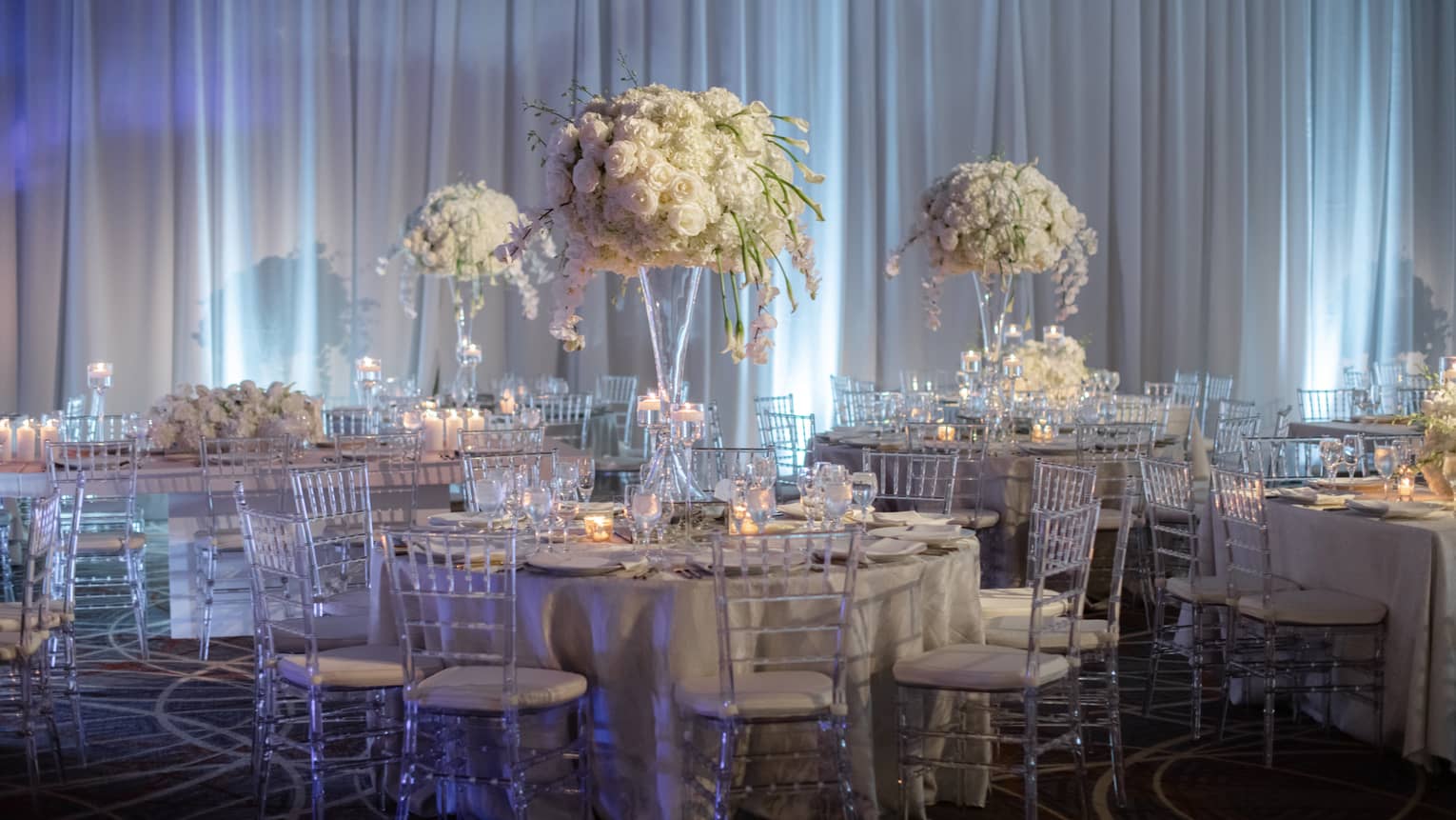 Dining tables in front of a curtain with large bouquets of flowers
