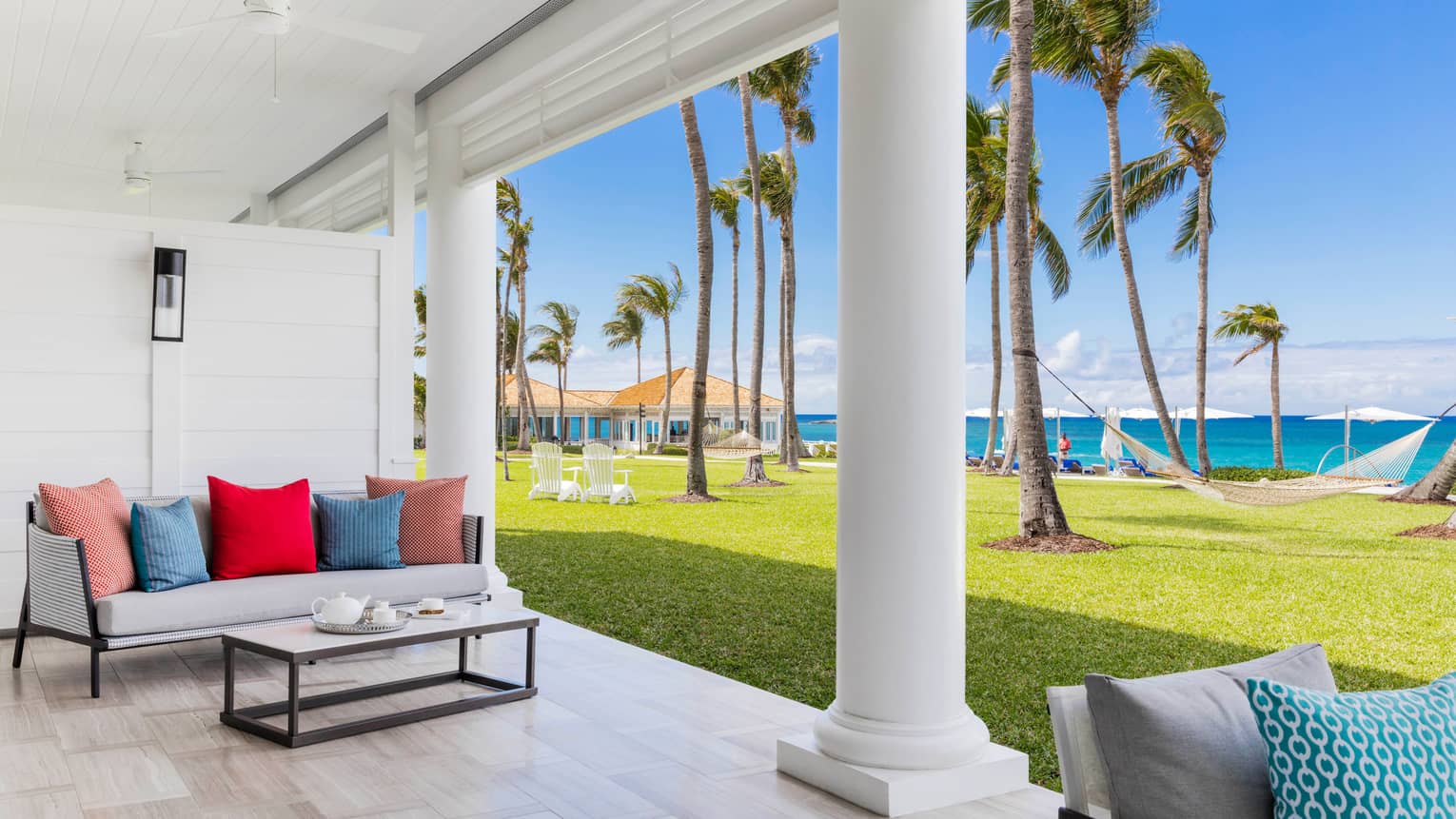 Patio sofa with colourful cushions under white pillars by lawn, ocean