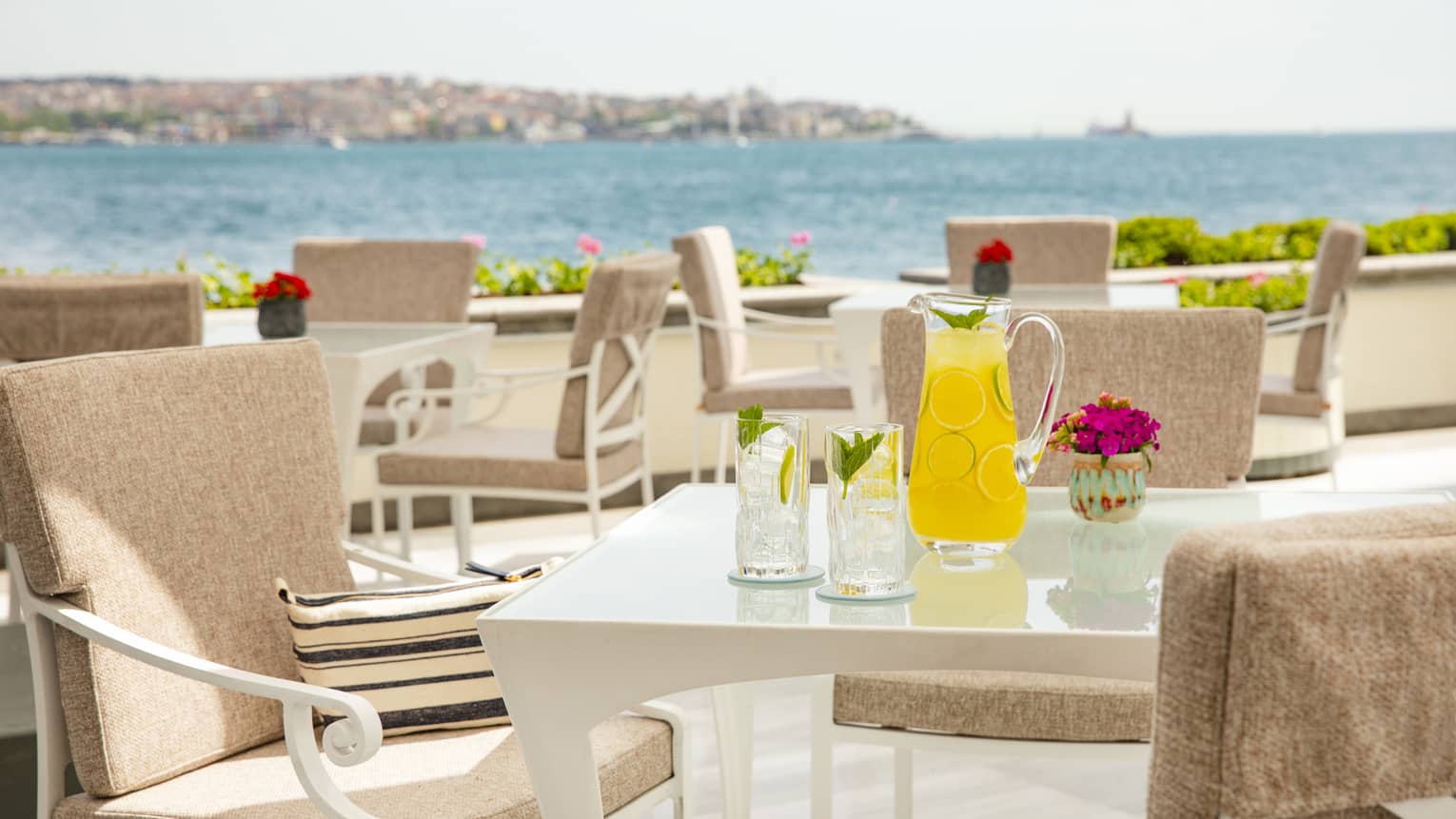 White dining tables and tan chairs on waterfront terrace