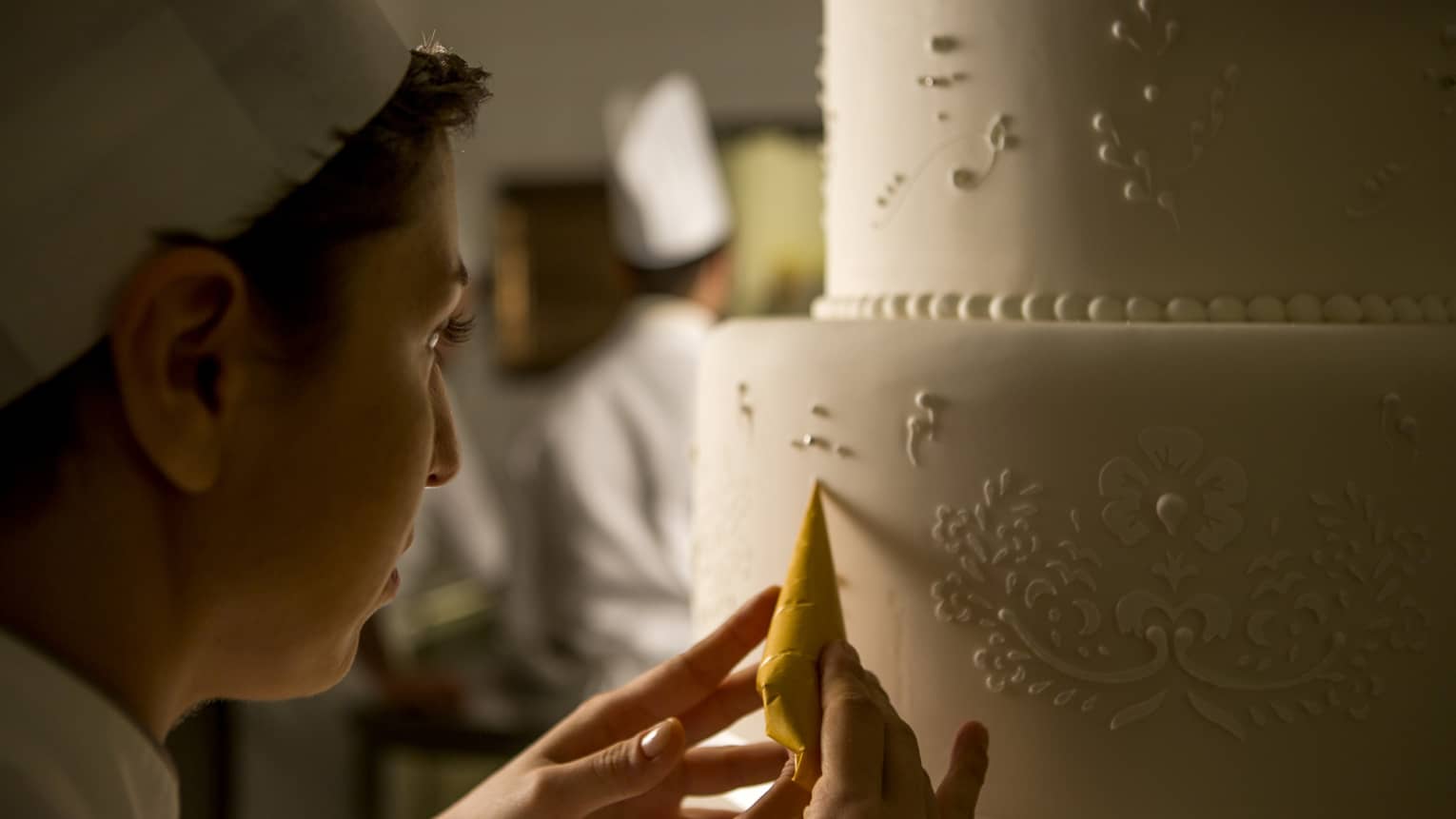 Pastry chef adds decorative details to tiered white wedding cake