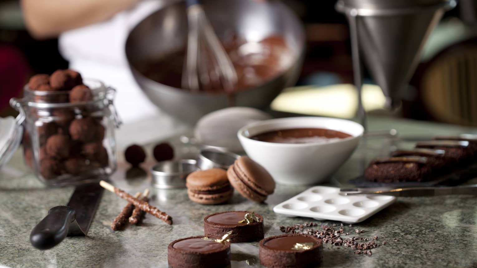 Close-up of fine chocolates, macarons, bowl of melted chocolate on counter