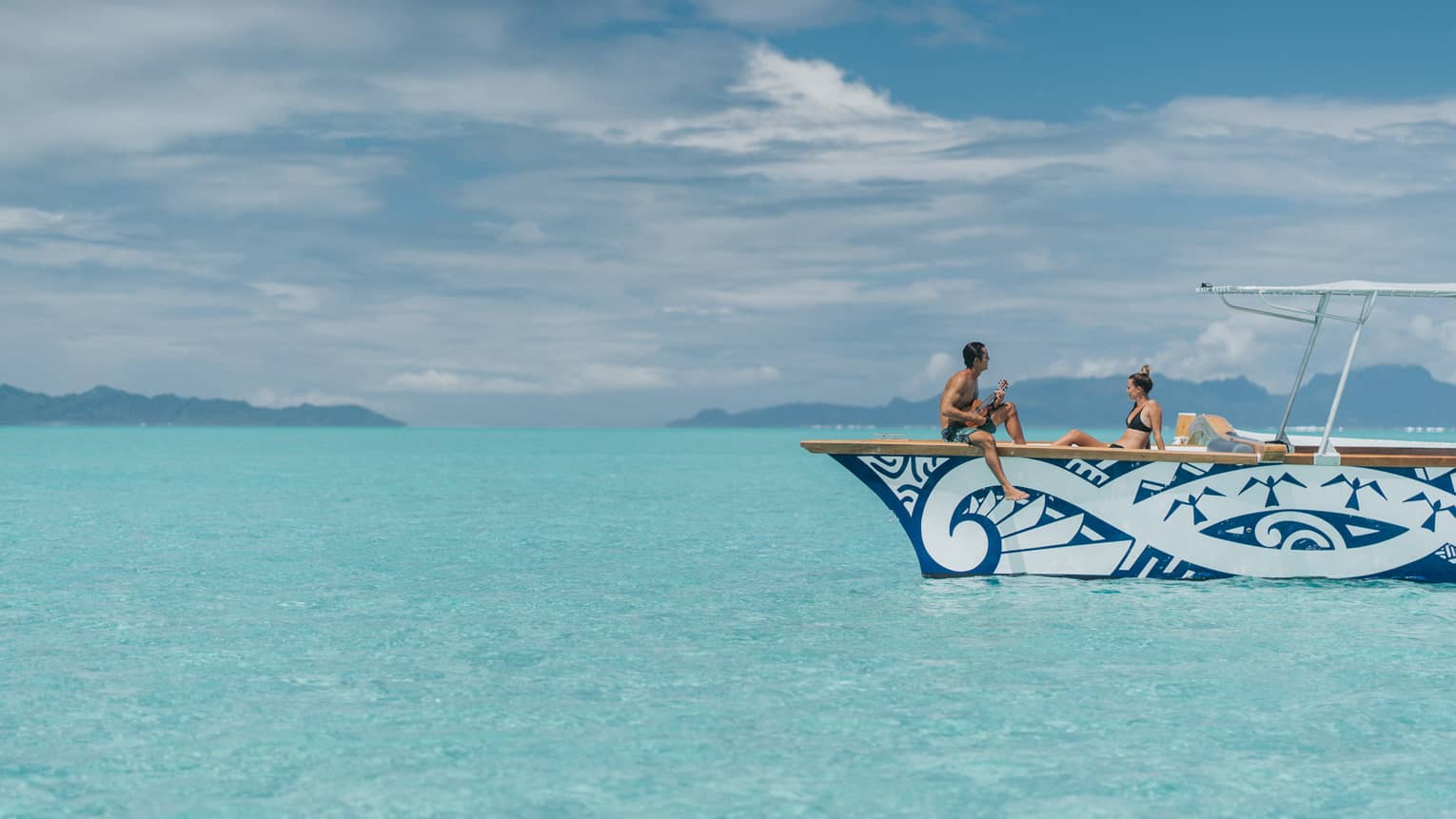 Man plays ukulele for woman on catamaran boat on lagoon