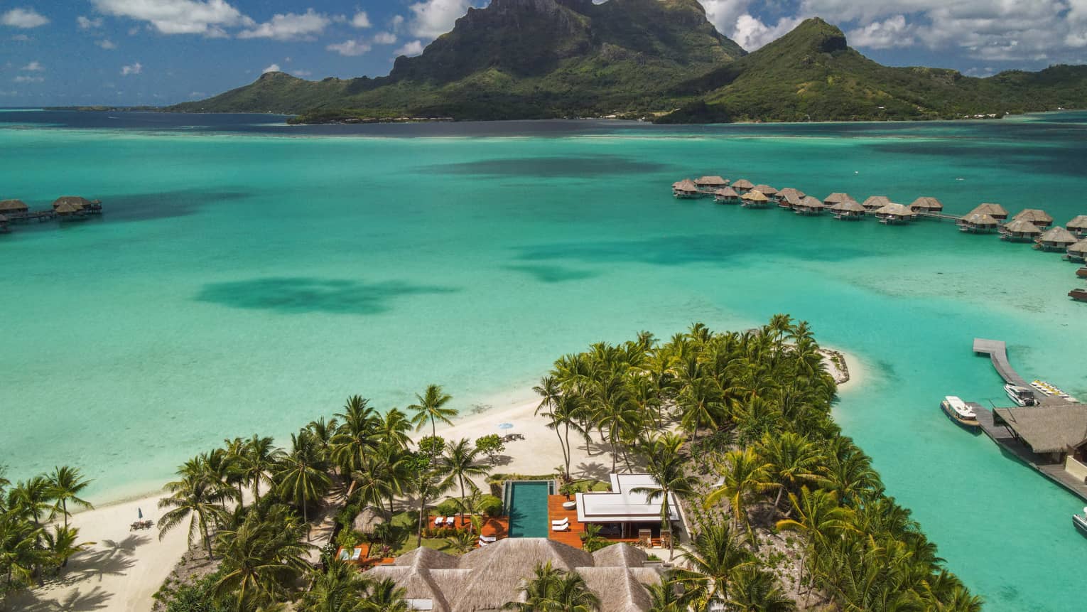 Aerial view of Bora Bora villa on edge of turquoise lagoon, looking out to overwater bungalows and mountains