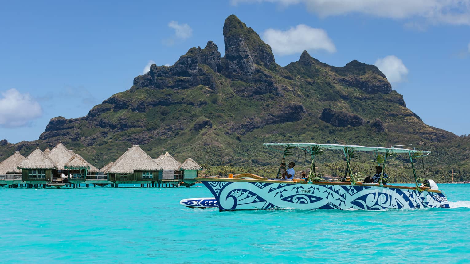 Blue and white patterned boat cruises along turquoise waters with lush green mountains in background