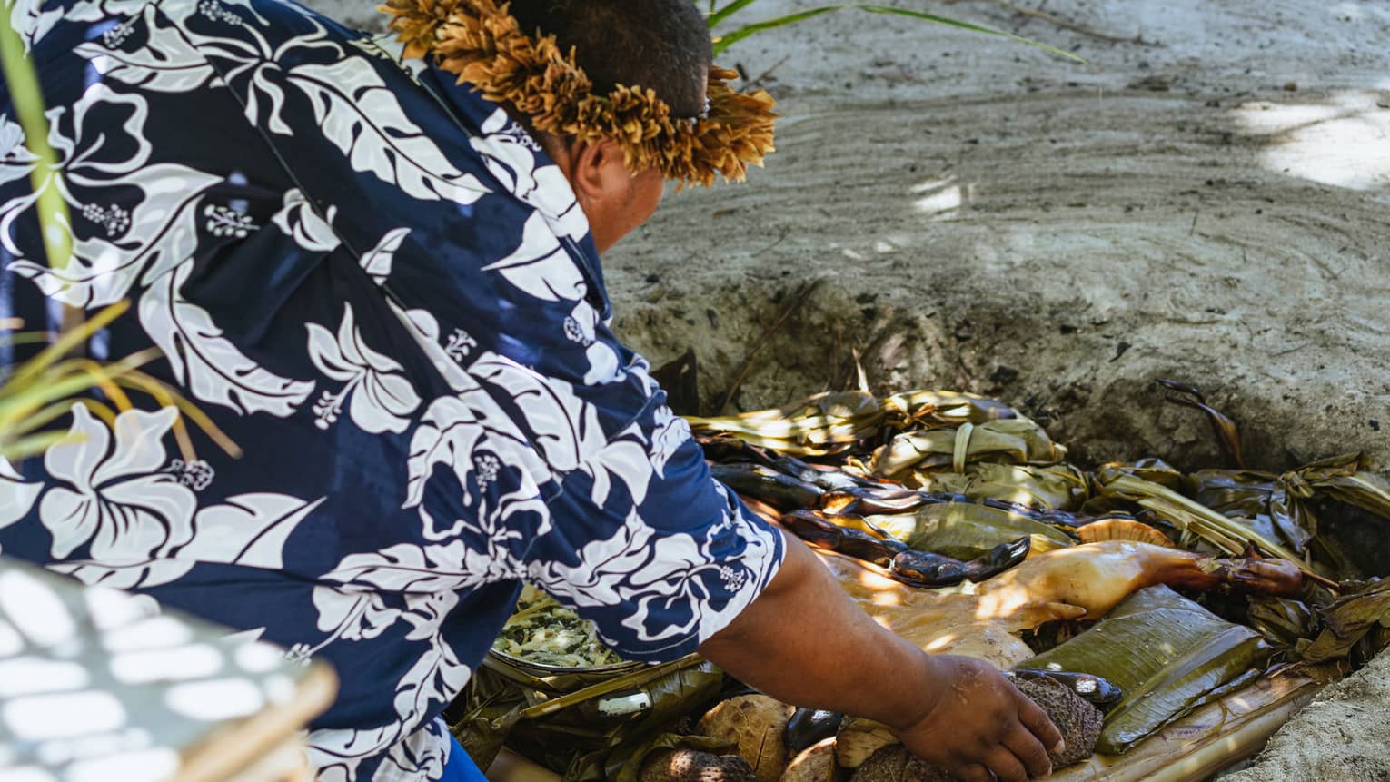 A chef places meat in a Tahitian oven: a hole dug into the sand filled with hot stones and palm leaves.