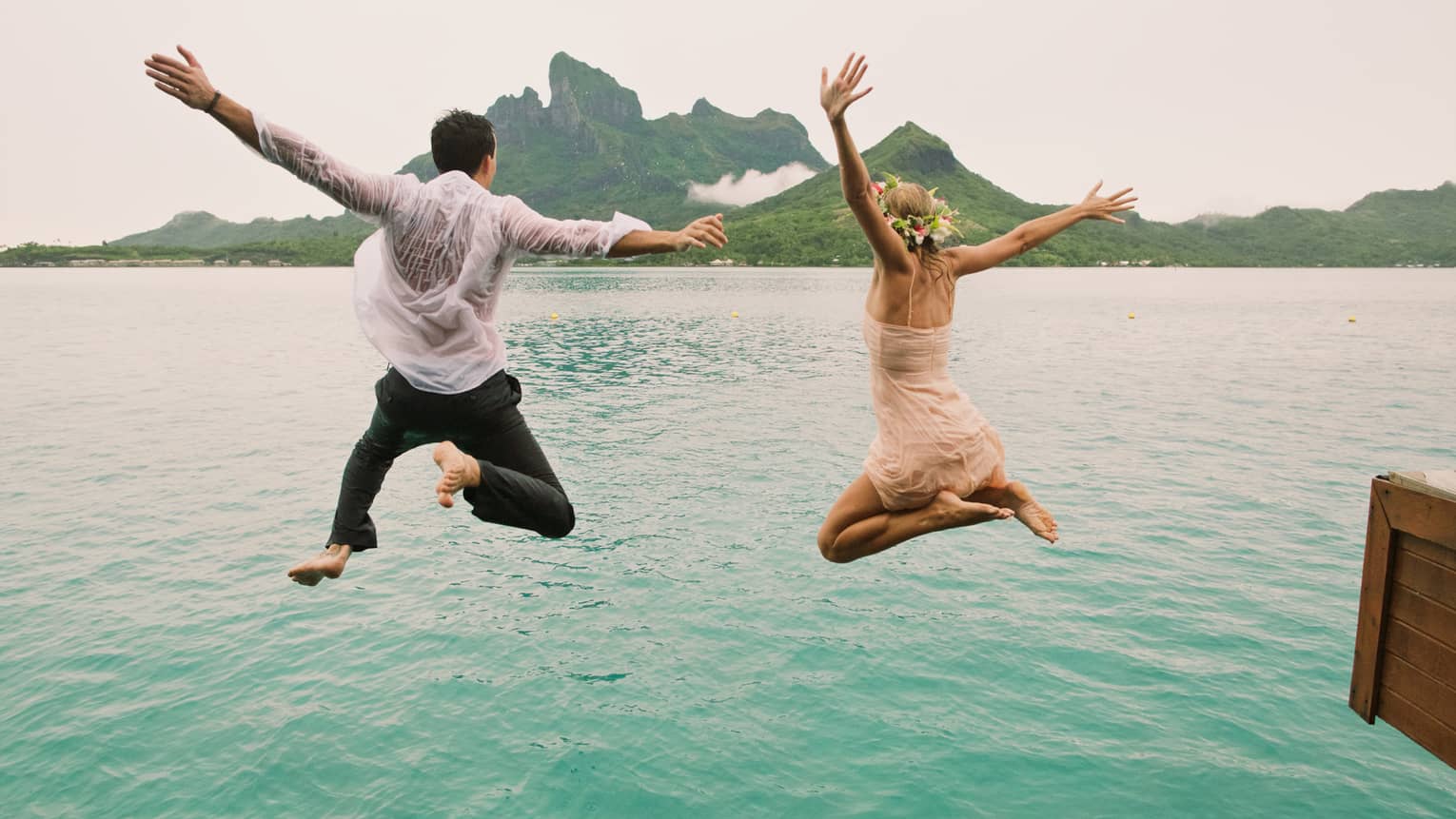 Woman and man in mid jump into turquoise lagoon