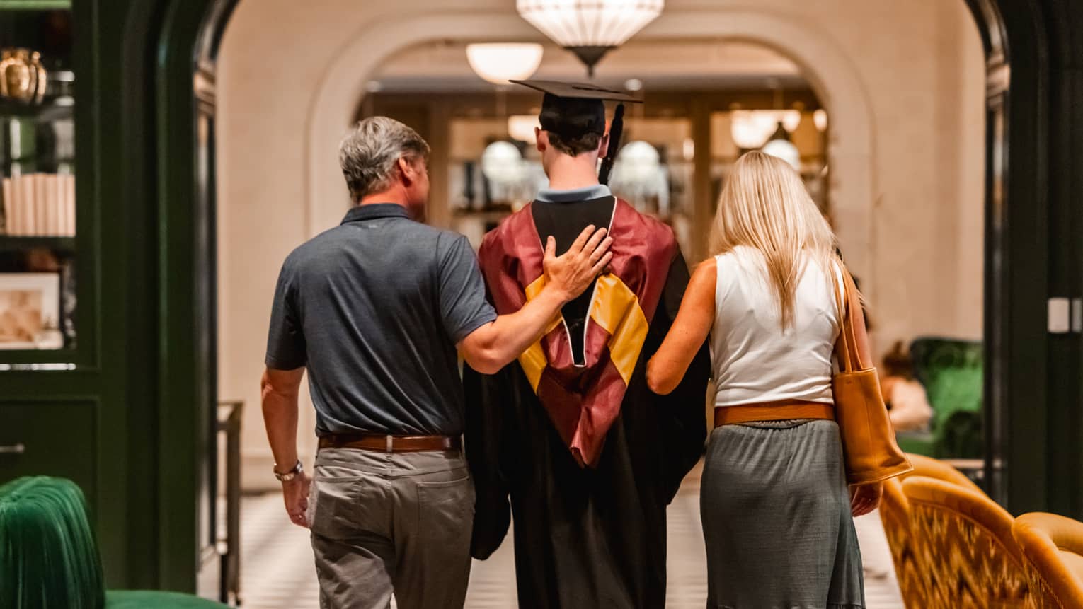 Parents walking with child in graduation gown.