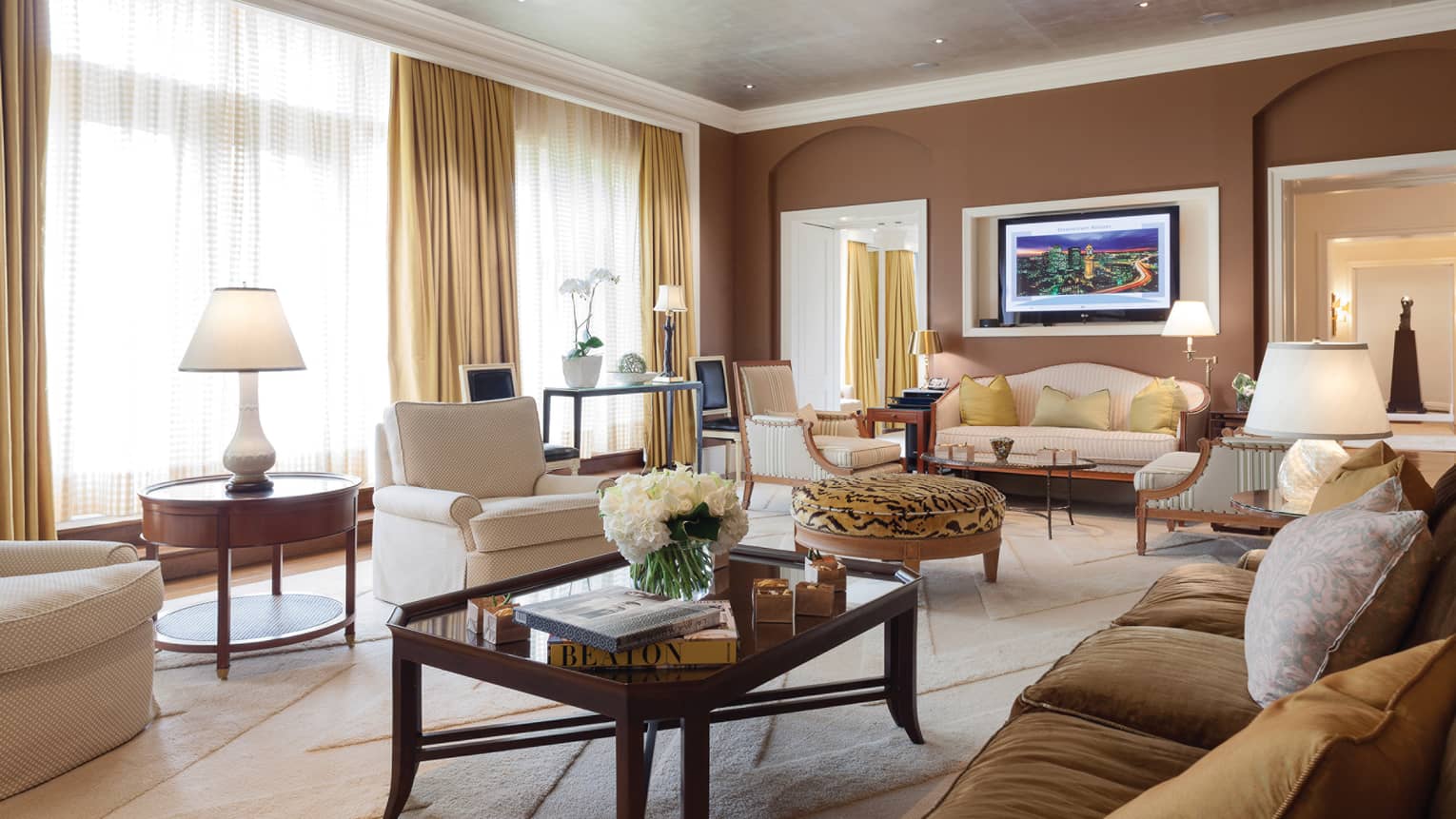 Presidential Suite living area coffee table with books and fresh white flowers, white armchair, tiger-print ottoman, sofas