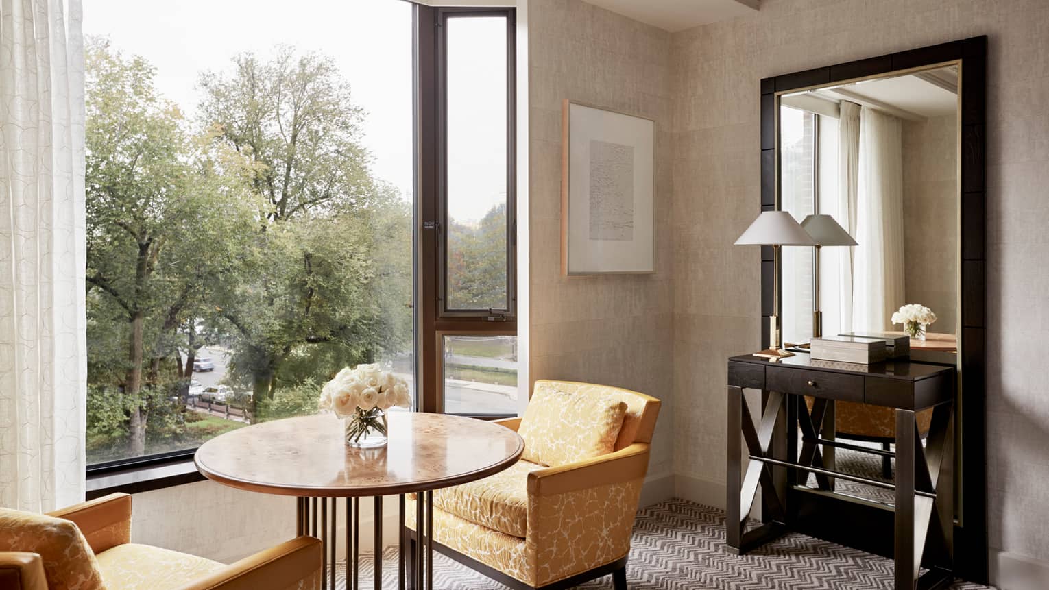 Deluxe Garden-View Room tall sunny window with view of trees, gold fabric armchairs at round table with fresh roses