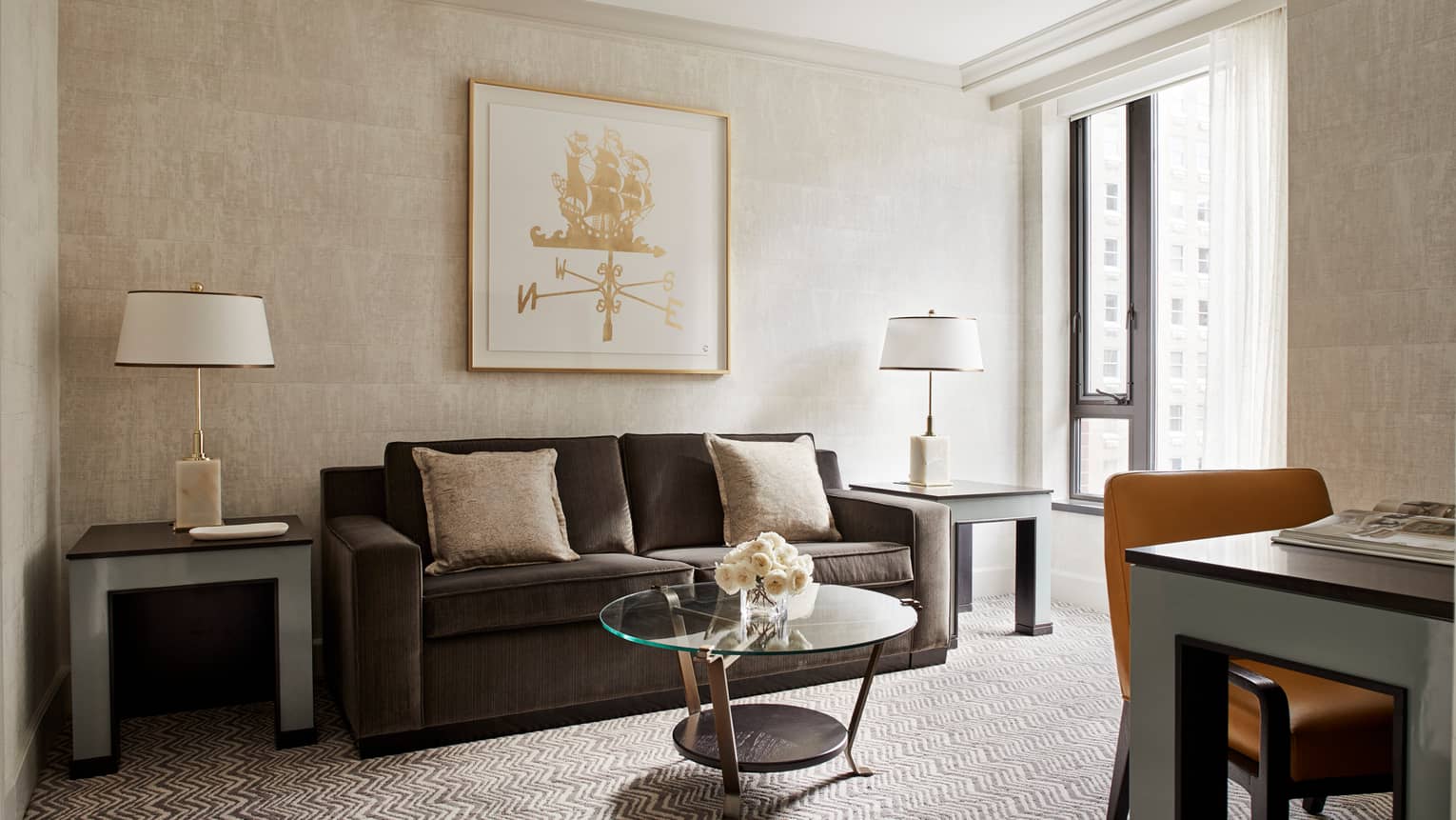 Four Seasons Executive Suite living room with dark grey sofa, beige pillows, framed gold print on wall, desk and sunny window