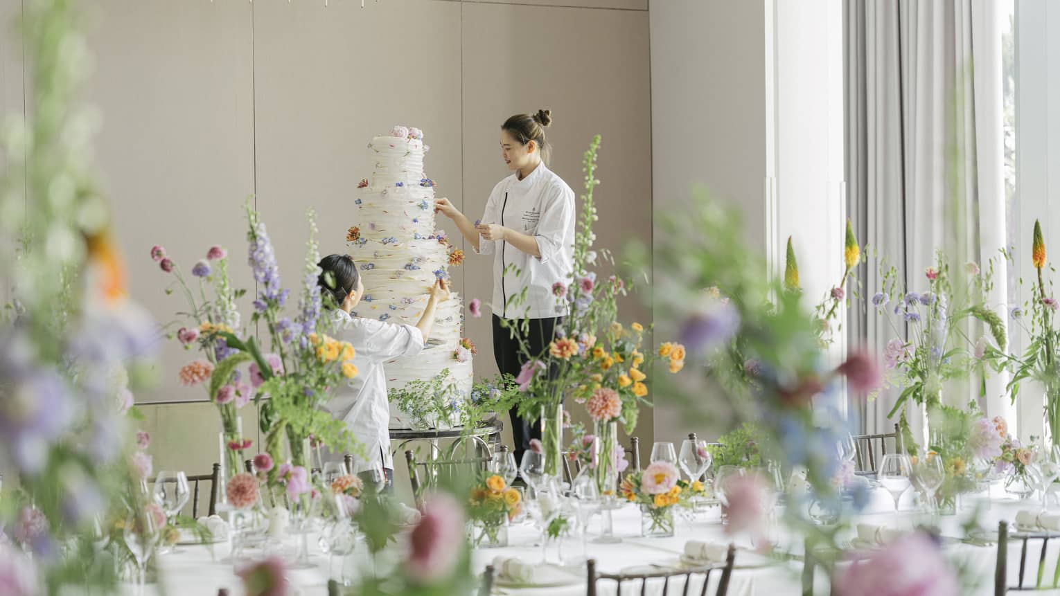 Two chefs decorate a five-tiered wedding cake in ballroom