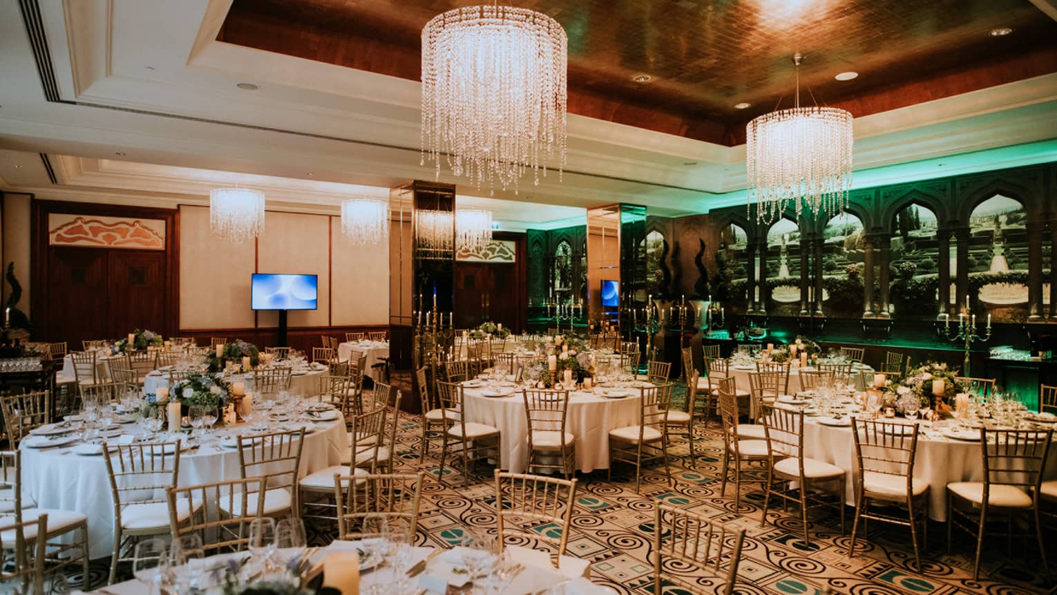 Round dining tables and chairs, flowers and candles in room with high ceilings and chandeliers