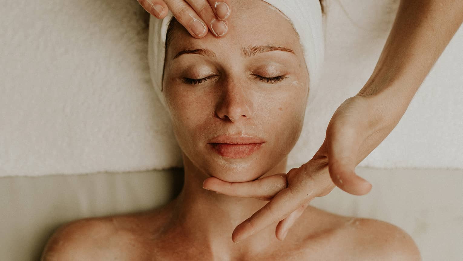 A woman reclines as a spa attendant performs a facial