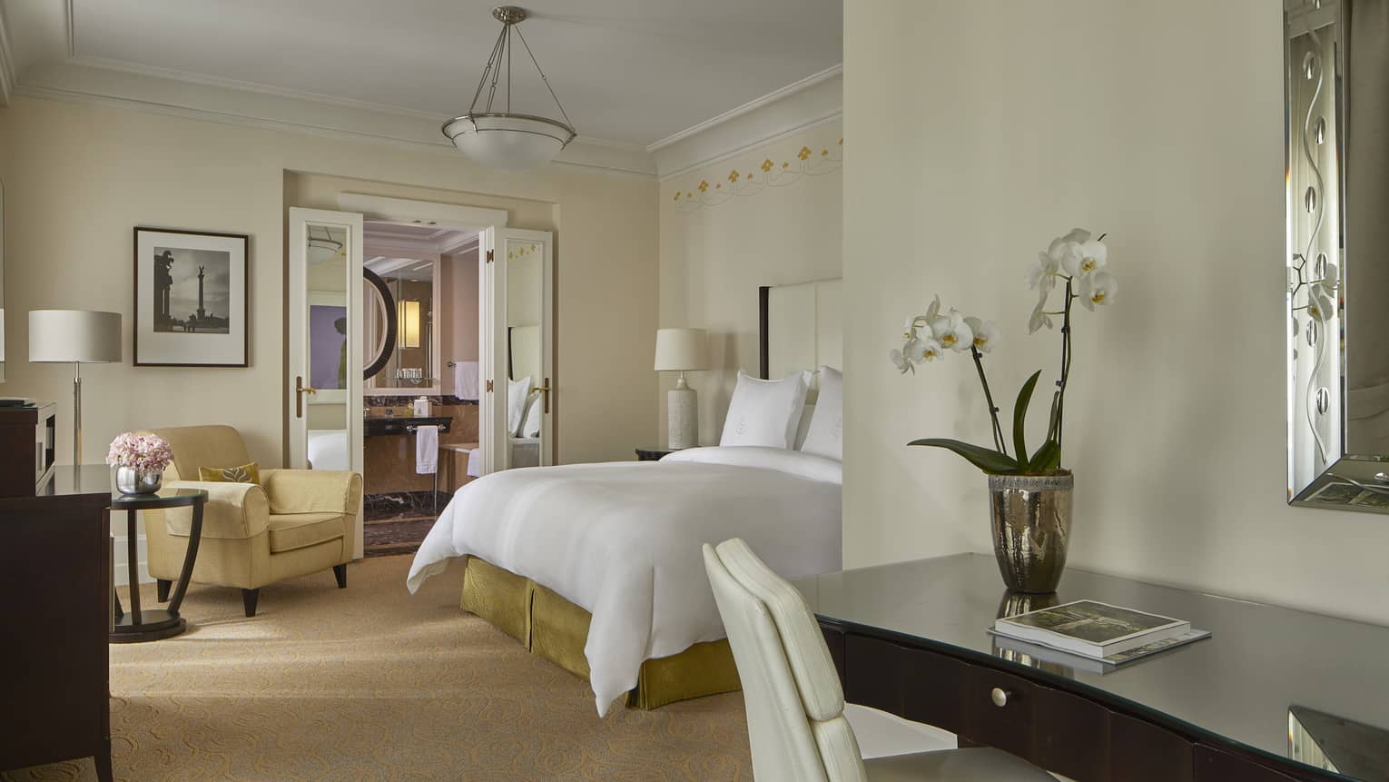 Elegant hotel room with white bed, orchid on desk and view into marble bathroom