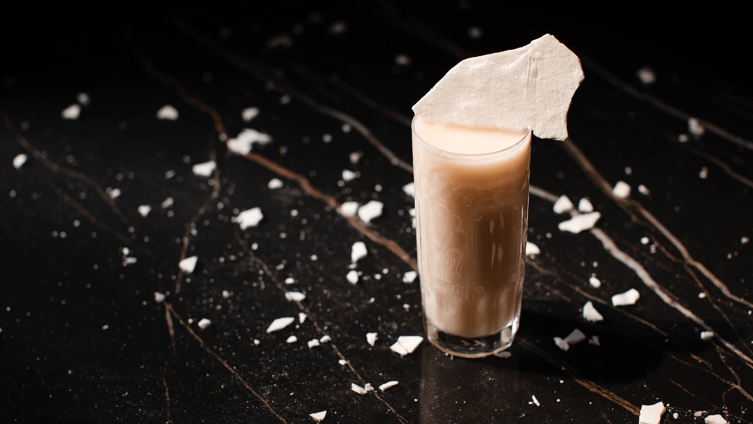 Frothy-looking ivory cocktail in highball glass on black speckled table