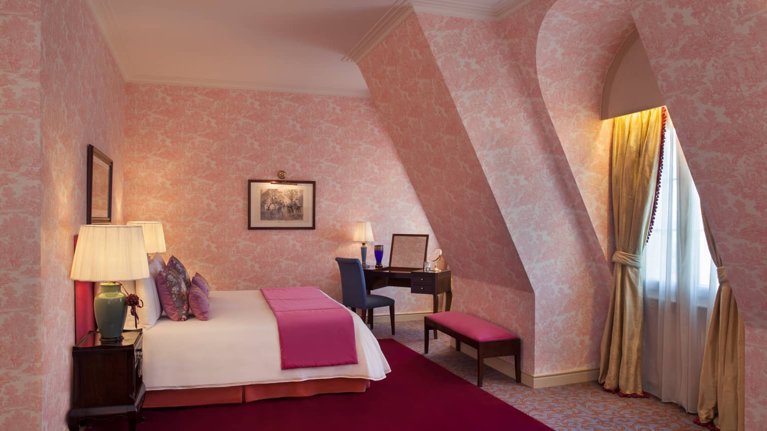 La Mansión Diplomatic Premier Suite with pink-patterned wallpaper on sloped walls, bed, bench and desk