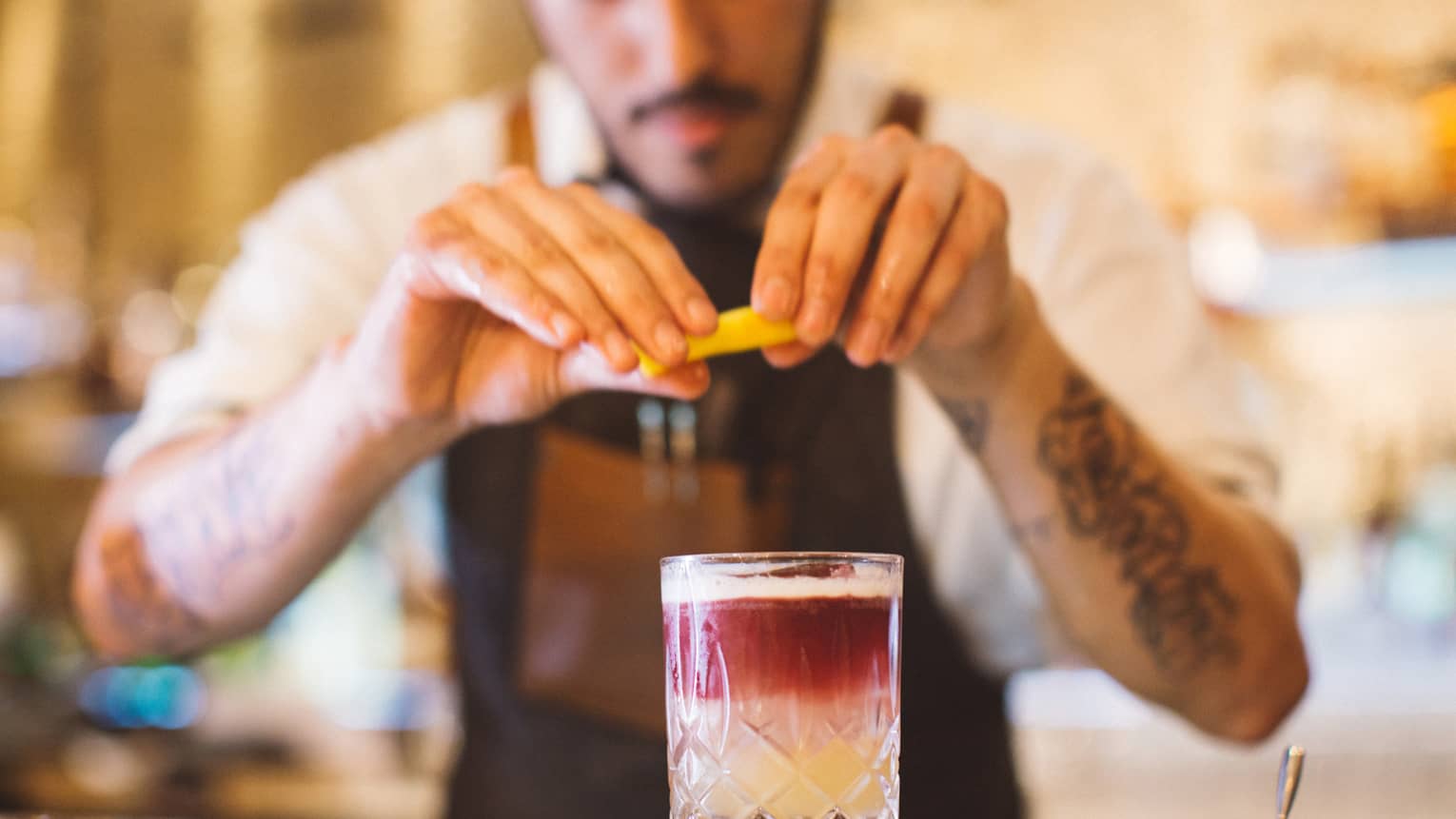 A bartender squeezes a lemon over a pink and white mixed drink. 