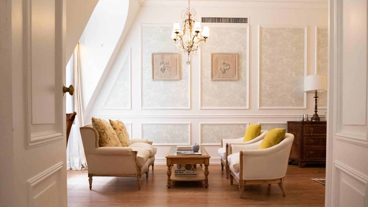 Living room with wooden floors, two white sofas facing each other with coffee table, small hanging chandelier