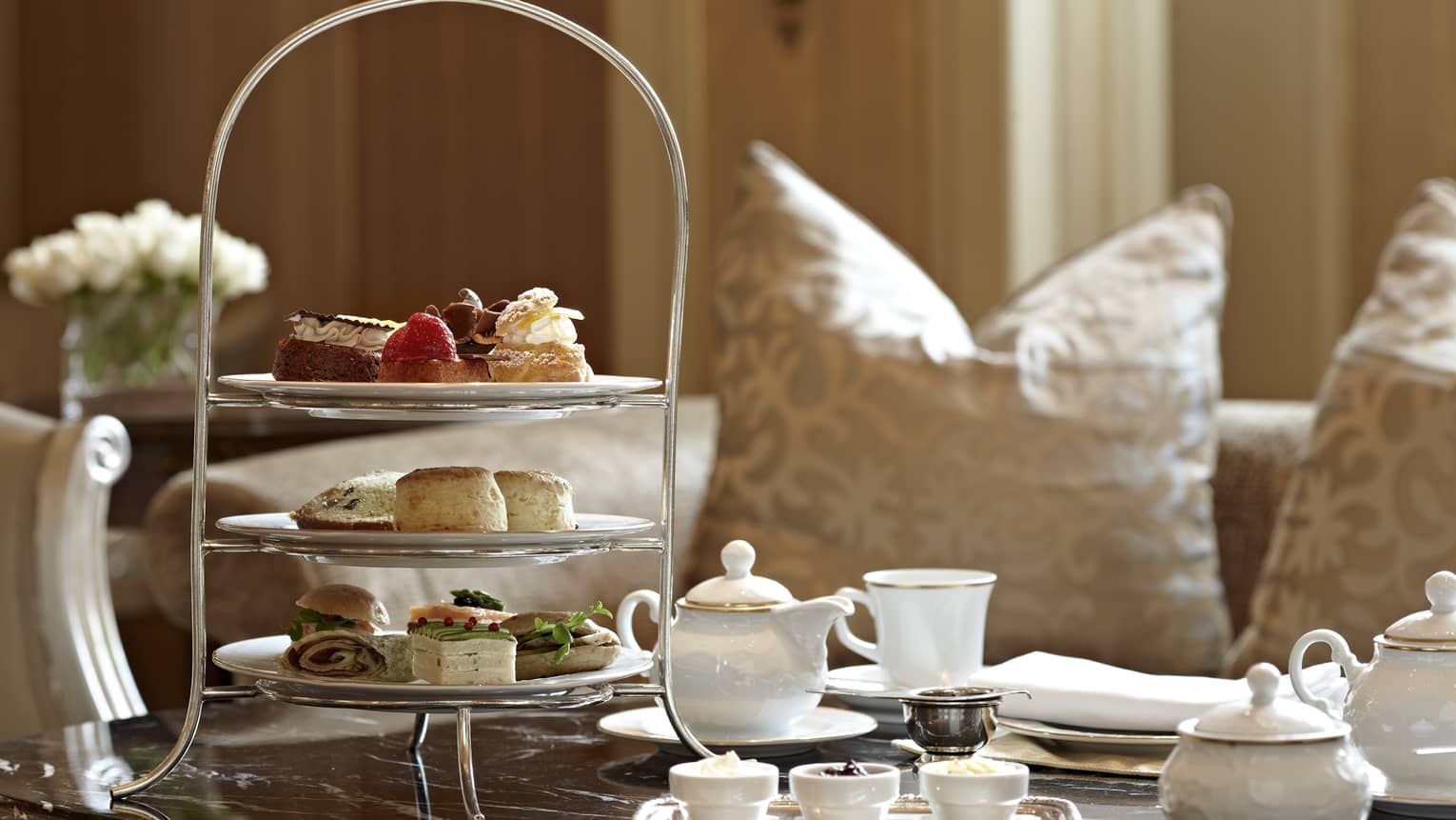 Formal tea setting on table with white teapot, tiered platter with sandwiches and desserts