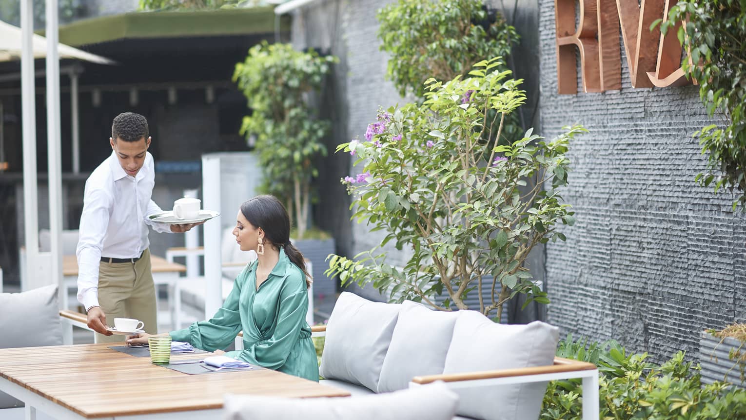 Woman in green dress seated at Riva restaurant terrace table, being served afternoon tea