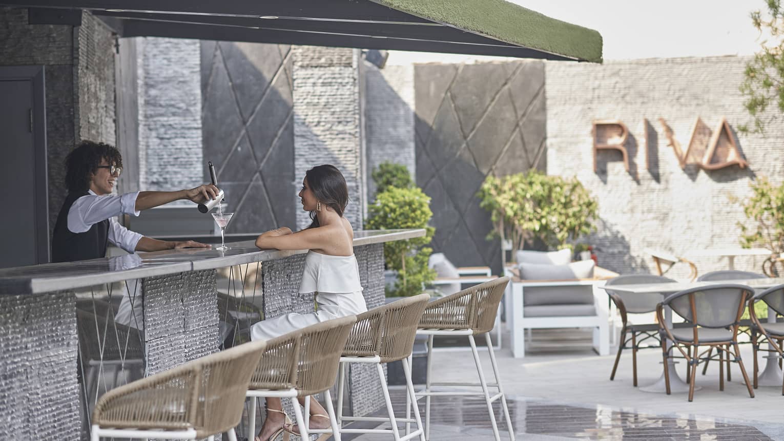 Woman seated at Riva restaurant terrace bar, being served a cocktail