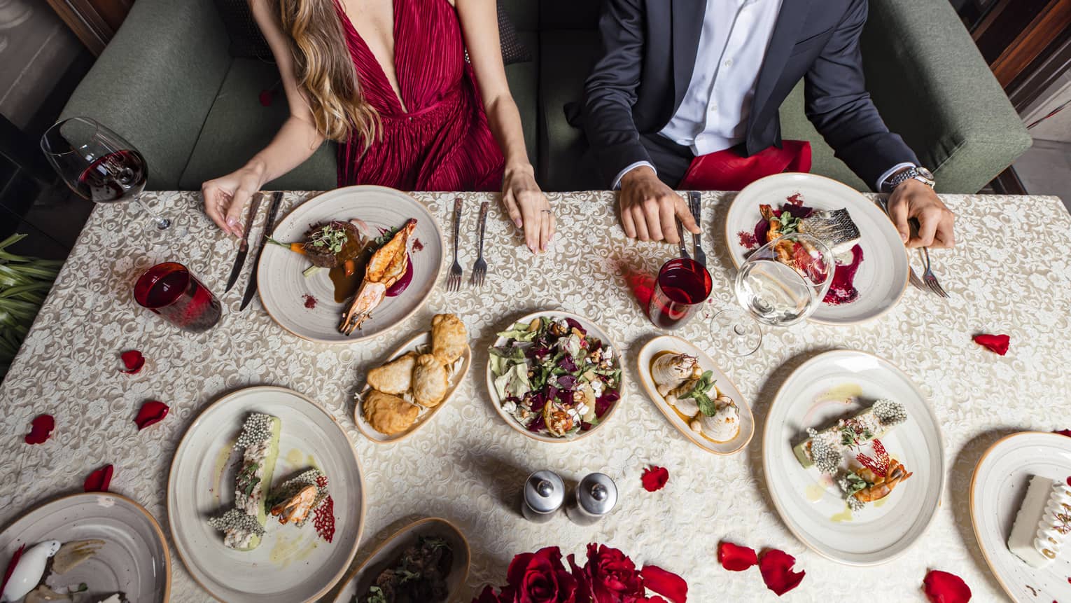 Aerial view of festive dishes on table with rose petals in front of couple