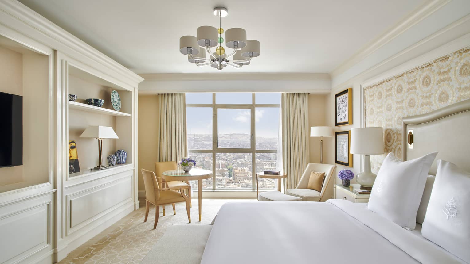 Hotel room with king bed and built-in wall shelves with TV, windowside sitting area