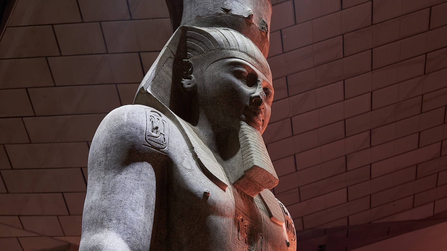 Close up of the head of a large statue of an Egyptian pharoah, lit from overhead in a museum.