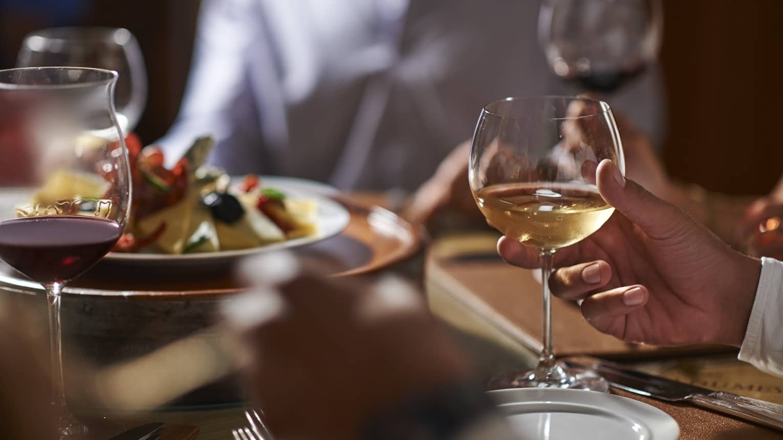 Close-up of hand holding wine glass by dinner plate on table