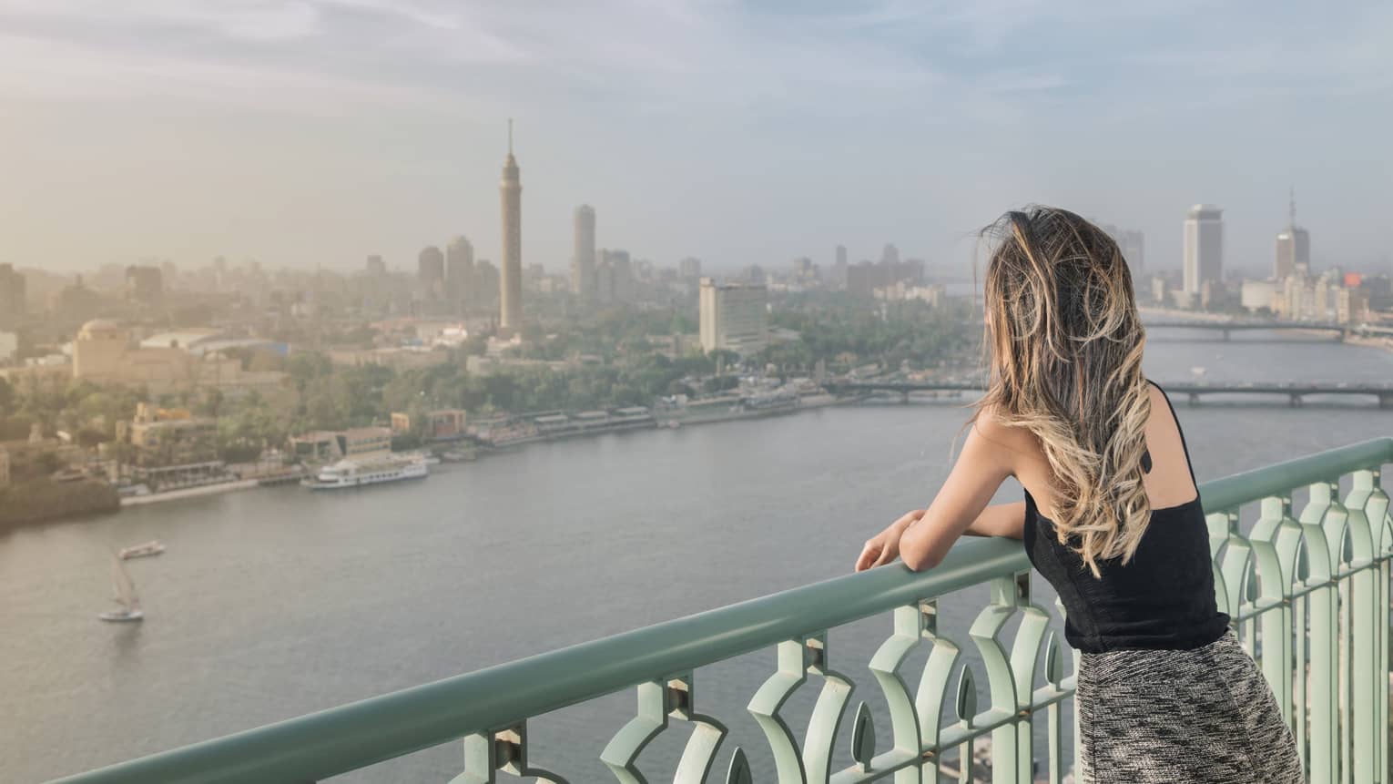 Woman with long blonde hair standing on balcony overlooking Nile River and Cairo