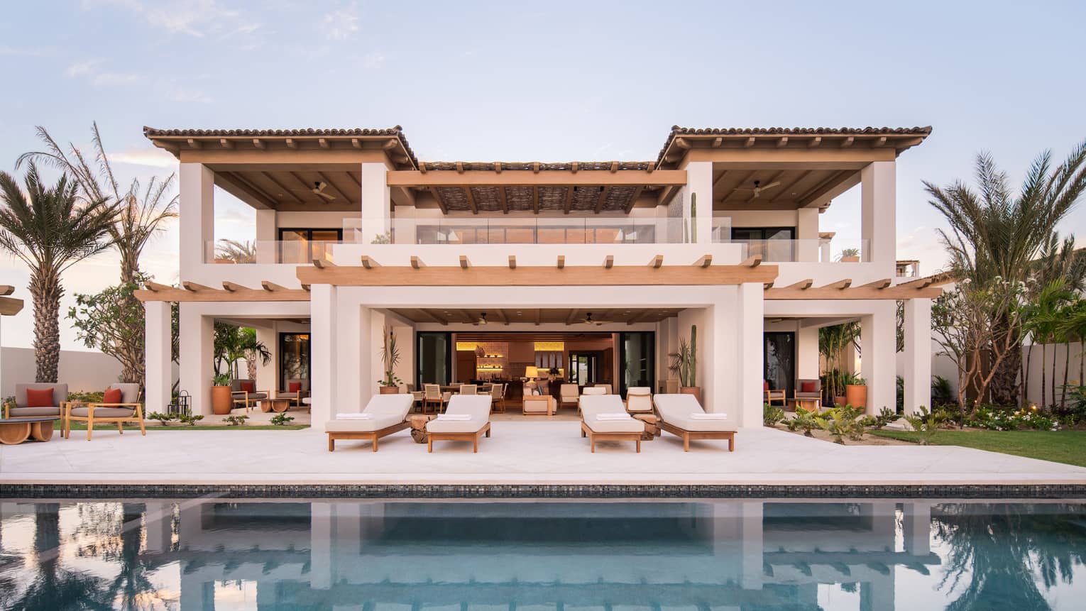 Spanish-style, two-storey villa lined by palm trees and sert behind a pool and deck