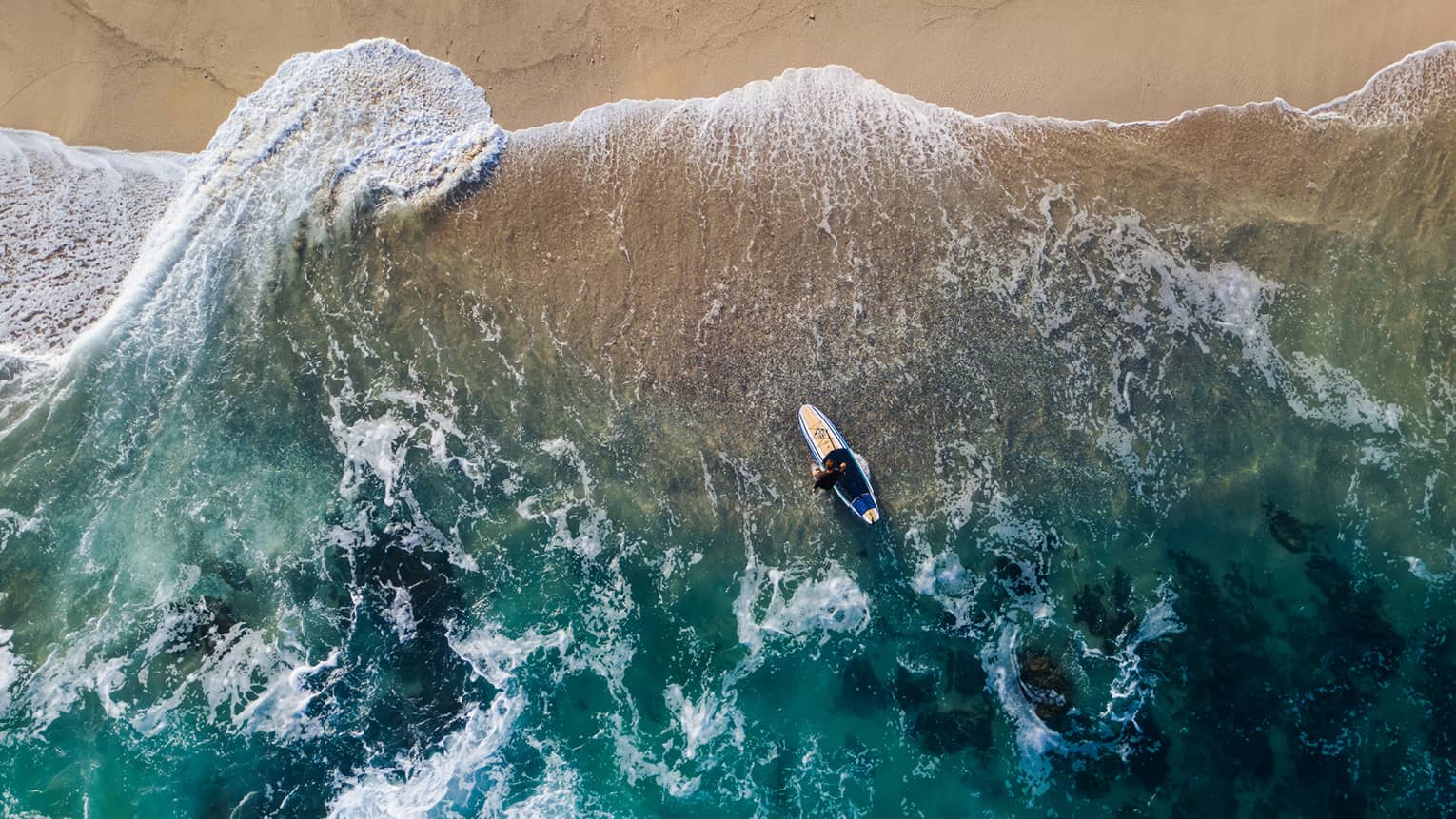 Aerial view of a person paddle boarding in the ocean by the beach