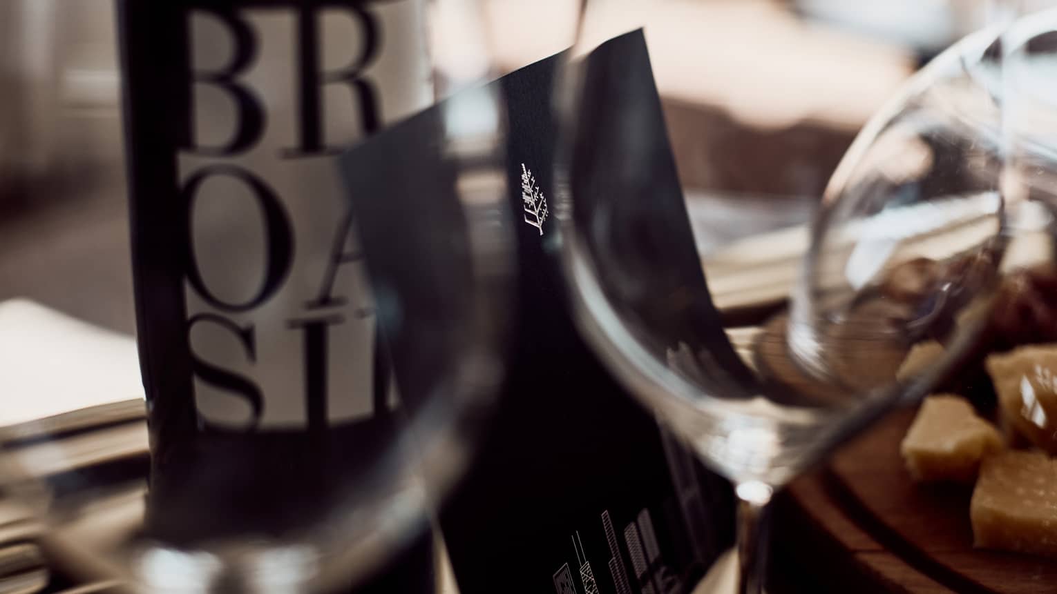 A Four Seasons menu propped up against a bottle of Portuguese red wine as seen through two wine glasses by a bowl of treats.